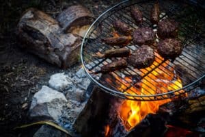 Burgers and sausages cooking on a grill over a camp fire