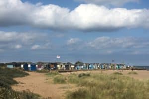 A sunny scene with blue skies looking over a row of beach huts at Chapel St Leonards